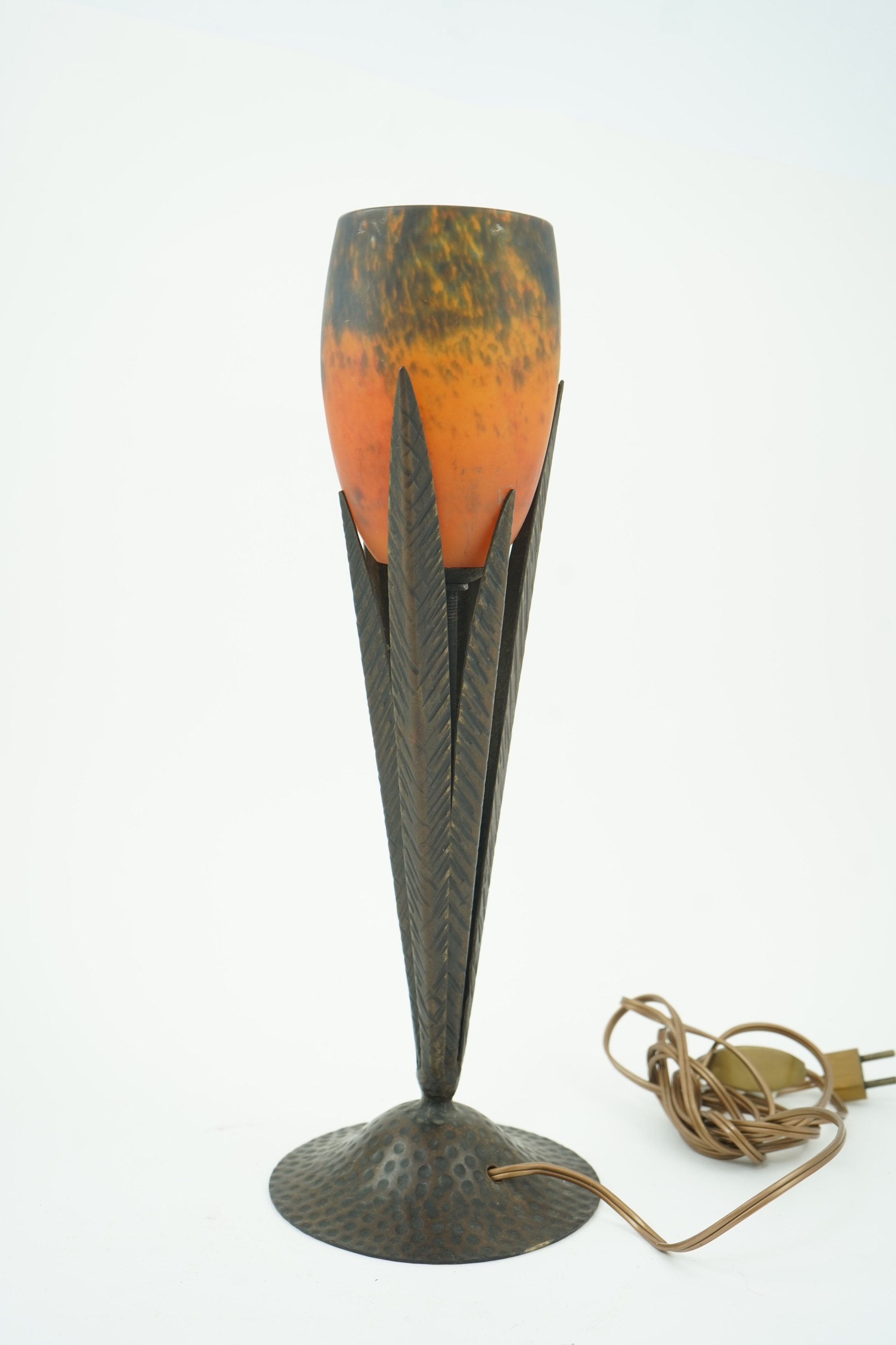 Manner of Muller Freres and Robj: A French Art Deco table lamp the mottled orange glass shade supported by naturalistic palm-leaf metal supports terminating in a circular hammered metal base, 40cm high
